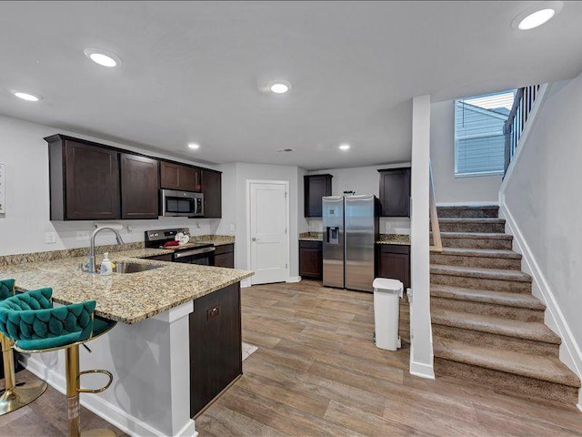 kitchen featuring stainless steel appliances, a sink, light stone countertops, dark brown cabinetry, and light wood-style floors