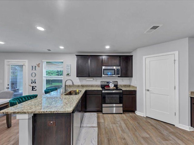 kitchen with stainless steel appliances, a sink, light wood-style floors, dark brown cabinets, and recessed lighting