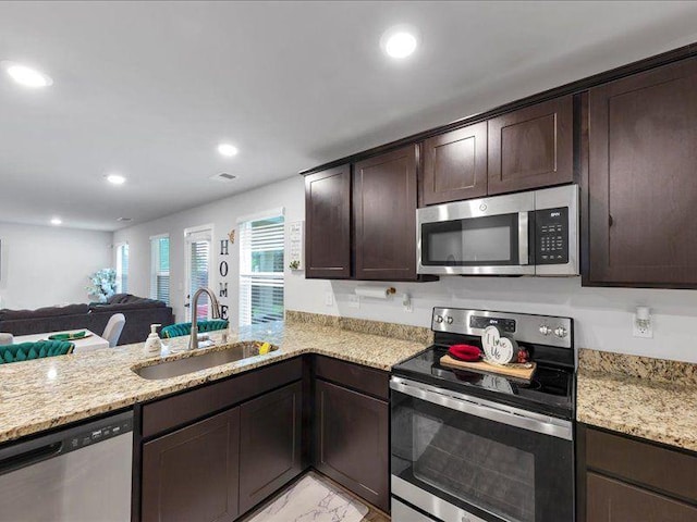 kitchen featuring stainless steel appliances, a sink, dark brown cabinets, light stone counters, and light marble finish floors