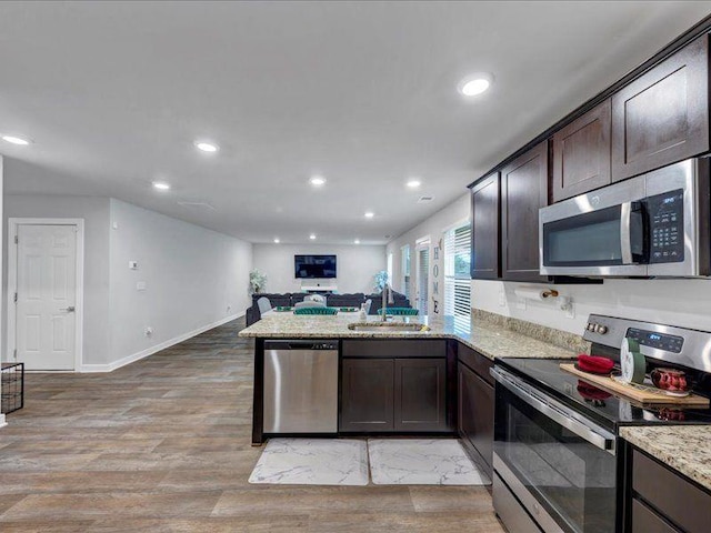 kitchen with stainless steel appliances, a peninsula, dark brown cabinets, open floor plan, and a sink