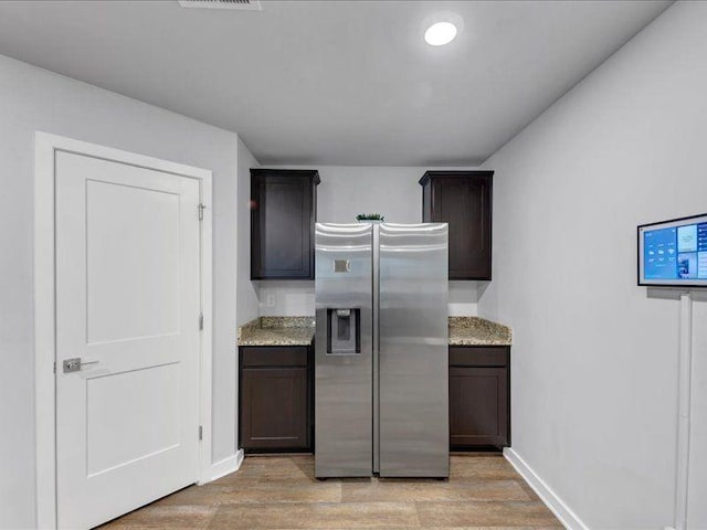 kitchen featuring stainless steel refrigerator with ice dispenser, light wood finished floors, dark brown cabinets, and light stone counters