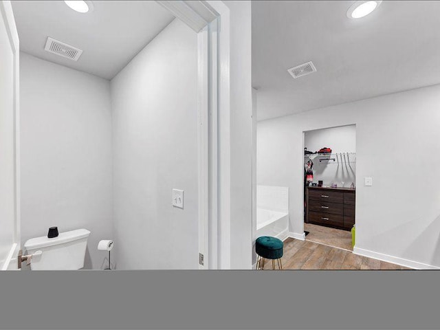 bathroom featuring toilet, wood finished floors, a bath, and baseboards