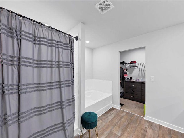 bathroom featuring wood finished floors, a garden tub, recessed lighting, a spacious closet, and baseboards