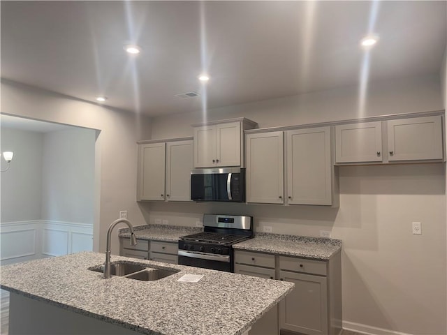 kitchen with gray cabinetry, appliances with stainless steel finishes, light stone countertops, and a sink