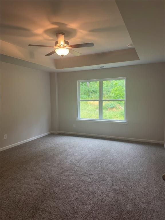 carpeted spare room with a tray ceiling, baseboards, and a ceiling fan