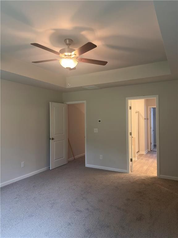 empty room with a ceiling fan, baseboards, a tray ceiling, and carpet