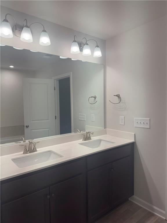full bathroom featuring a sink, double vanity, baseboards, and wood finished floors