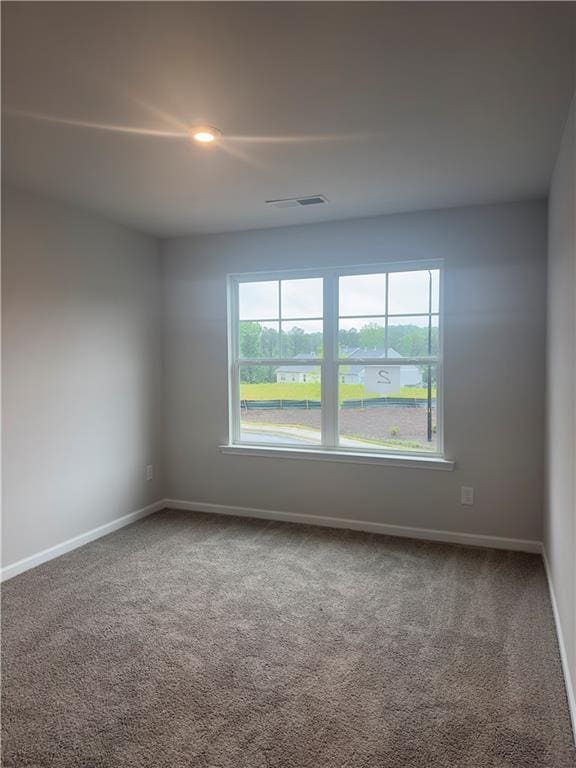 carpeted spare room featuring visible vents, baseboards, and a healthy amount of sunlight