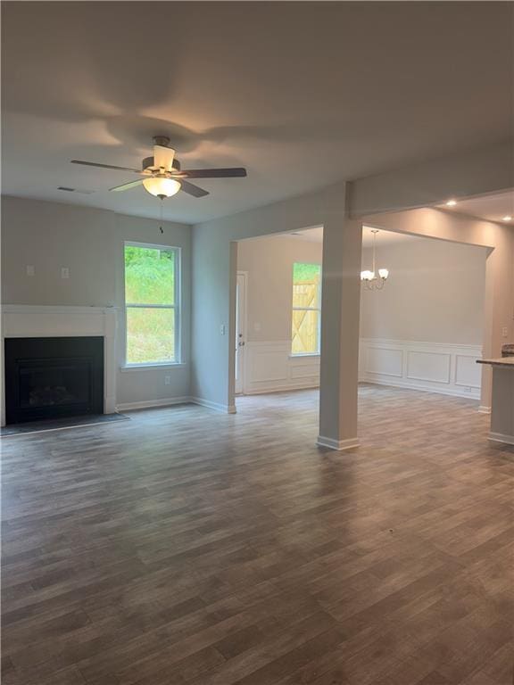 unfurnished living room featuring ceiling fan with notable chandelier, a decorative wall, a fireplace with flush hearth, and dark wood-type flooring