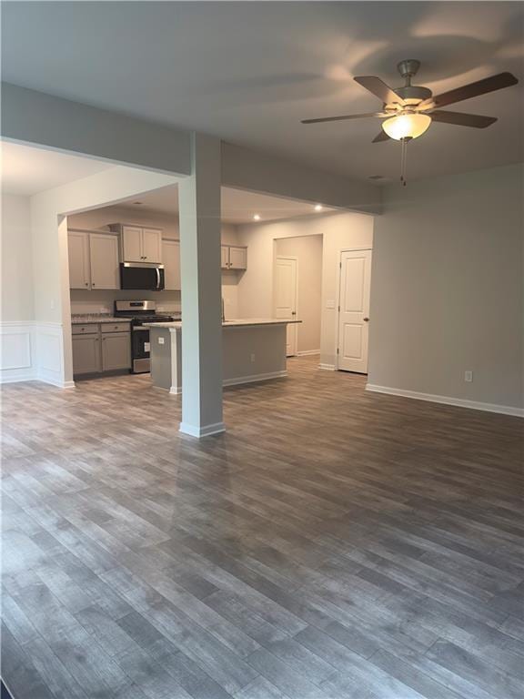 unfurnished living room featuring baseboards, wainscoting, ceiling fan, and dark wood-type flooring