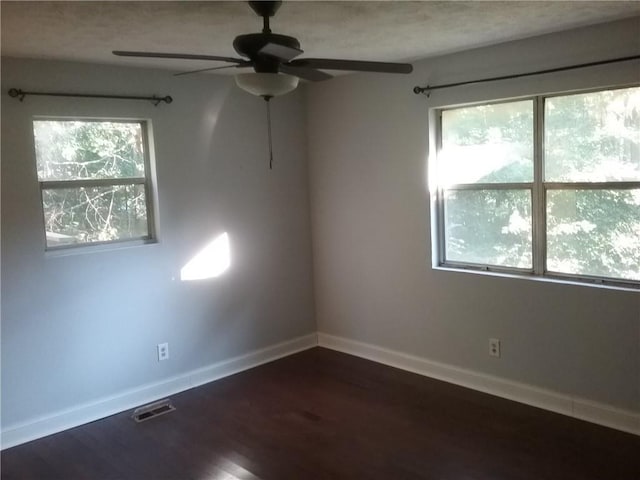 unfurnished room with dark wood finished floors, plenty of natural light, baseboards, and visible vents