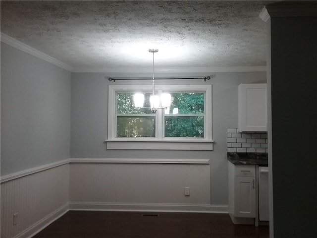 unfurnished dining area featuring ornamental molding, a textured ceiling, dark wood finished floors, an inviting chandelier, and wainscoting