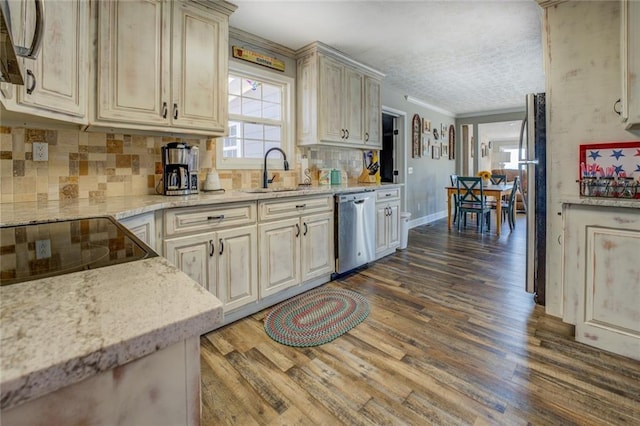 kitchen with wood finished floors, a sink, appliances with stainless steel finishes, cream cabinetry, and light stone countertops