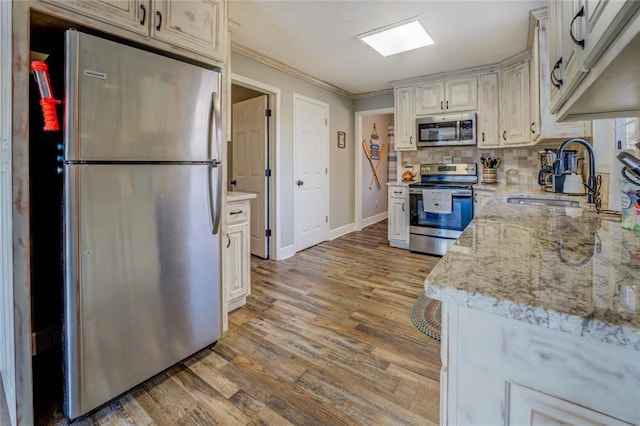 kitchen with appliances with stainless steel finishes, light stone counters, ornamental molding, light wood-type flooring, and a sink