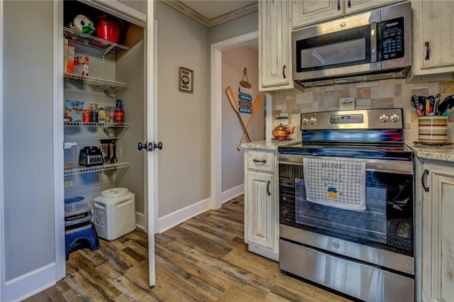 kitchen featuring baseboards, decorative backsplash, appliances with stainless steel finishes, ornamental molding, and wood finished floors