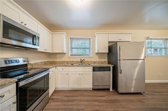 kitchen with appliances with stainless steel finishes, a wealth of natural light, sink, white cabinets, and light stone countertops