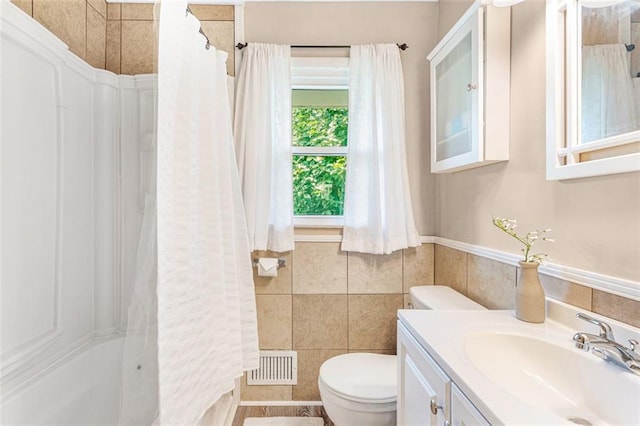 full bathroom with tile walls, visible vents, toilet, wainscoting, and vanity