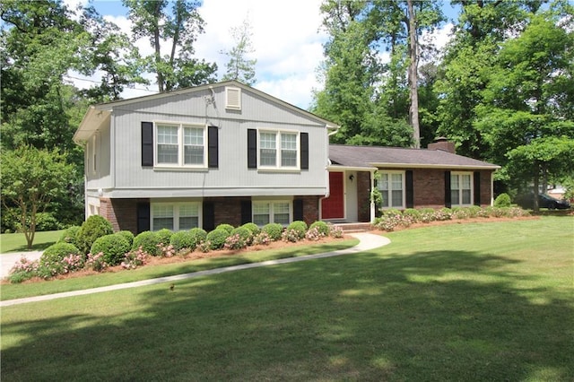 split level home with brick siding, a chimney, and a front yard