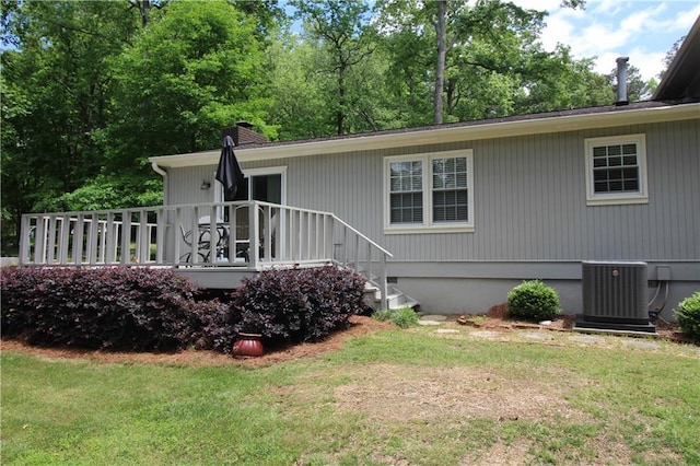 back of house featuring central air condition unit, a wooden deck, a chimney, and a lawn
