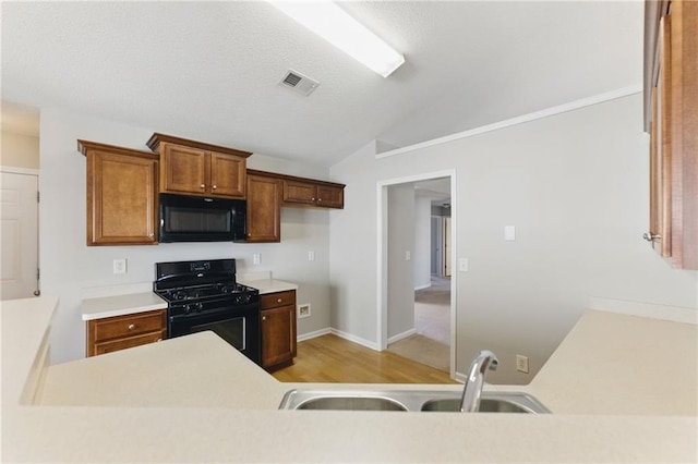 kitchen featuring lofted ceiling, a sink, visible vents, light countertops, and black appliances