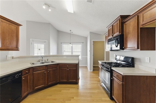 kitchen with lofted ceiling, light wood-style flooring, a peninsula, a sink, and black appliances