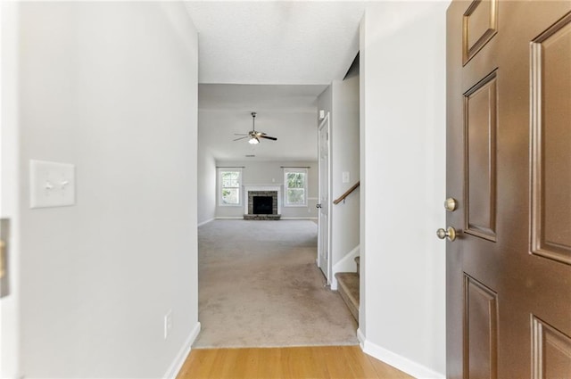 hall featuring light carpet, light wood-style flooring, stairs, and baseboards