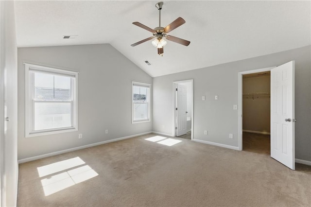 unfurnished bedroom featuring lofted ceiling, carpet, a walk in closet, and baseboards