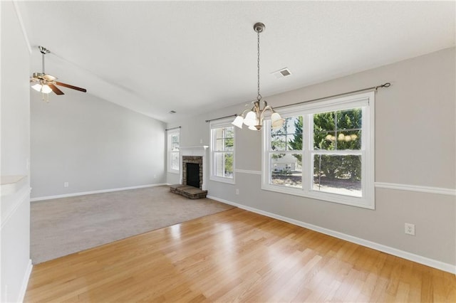 unfurnished living room with ceiling fan with notable chandelier, a fireplace, visible vents, baseboards, and vaulted ceiling