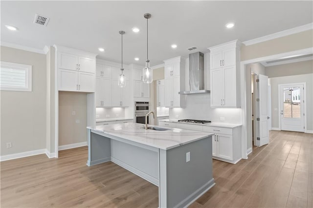 kitchen with a center island with sink, wall chimney exhaust hood, light stone counters, and white cabinets