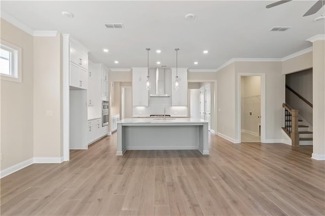 kitchen featuring light hardwood / wood-style flooring, a kitchen island with sink, wall chimney range hood, and white cabinetry