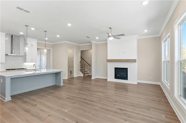 kitchen with light hardwood / wood-style floors, wall chimney exhaust hood, white cabinets, and decorative light fixtures