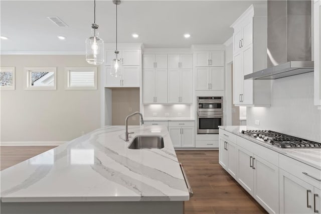 kitchen featuring a large island with sink, sink, white cabinets, wall chimney range hood, and appliances with stainless steel finishes