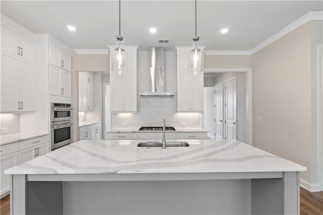 kitchen featuring wall chimney exhaust hood, light stone counters, pendant lighting, and a large island with sink