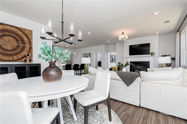 dining area featuring visible vents, a glass covered fireplace, wood finished floors, a chandelier, and recessed lighting