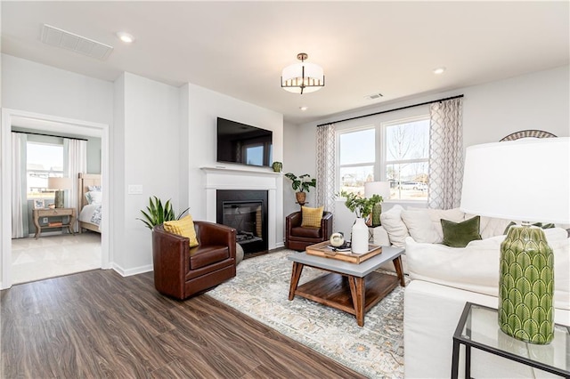 living area featuring plenty of natural light, visible vents, dark wood-type flooring, and a glass covered fireplace