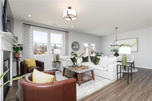 living room with french doors, dark wood finished floors, a glass covered fireplace, a chandelier, and baseboards