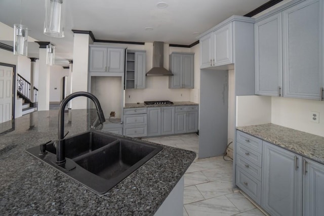 kitchen featuring wall chimney range hood, stainless steel gas cooktop, dark stone countertops, marble finish floor, and a sink