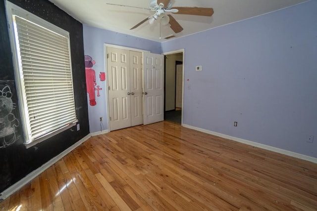 unfurnished bedroom featuring visible vents, a closet, wood-type flooring, baseboards, and ceiling fan