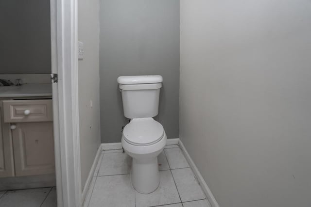 half bathroom with vanity, tile patterned floors, toilet, and baseboards