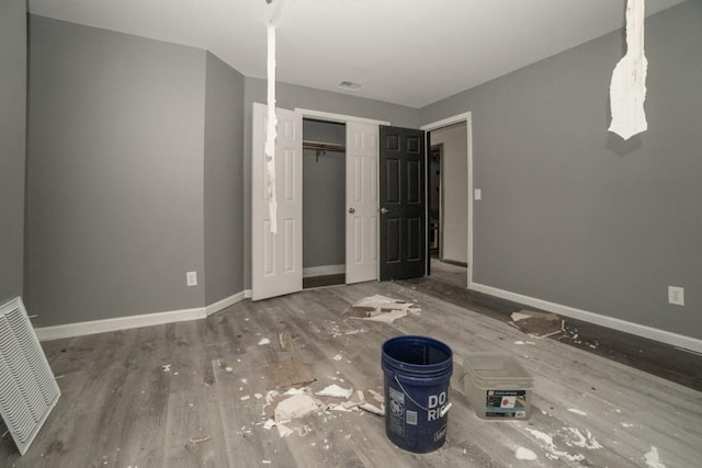 unfurnished bedroom featuring wood finished floors, baseboards, visible vents, and a closet