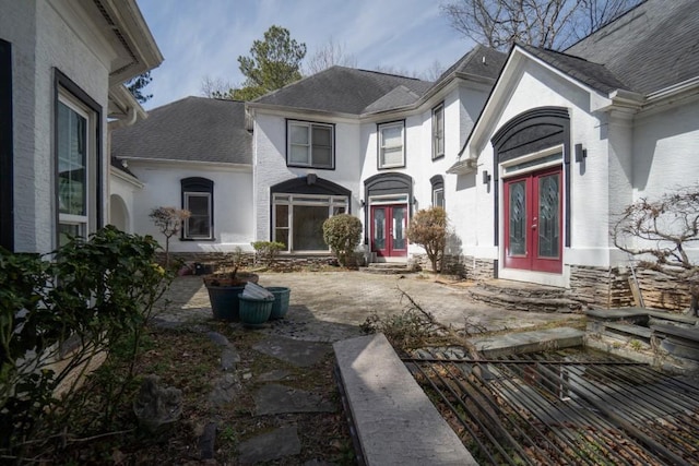 exterior space with a shingled roof, french doors, and stucco siding