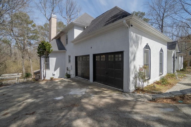 view of property exterior with stucco siding, driveway, a chimney, and a garage