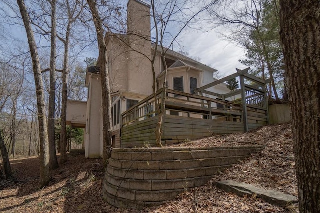 back of property featuring stairs, a wooden deck, a chimney, and stucco siding