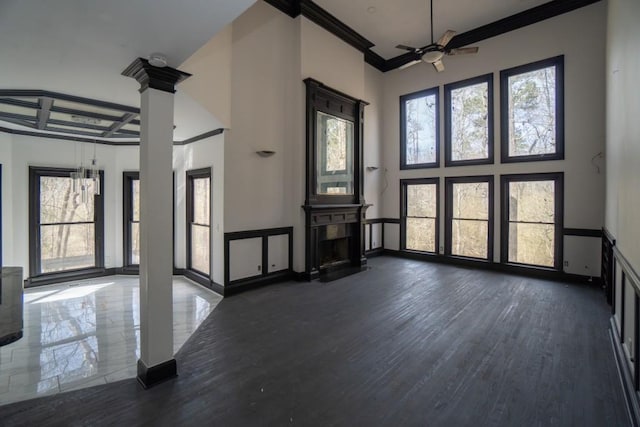 unfurnished living room with a fireplace with flush hearth, plenty of natural light, crown molding, and ornate columns