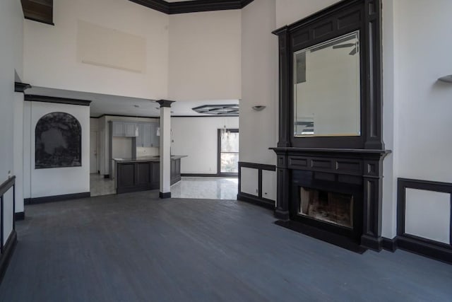 unfurnished living room with a fireplace with flush hearth, ornamental molding, wood finished floors, decorative columns, and a towering ceiling