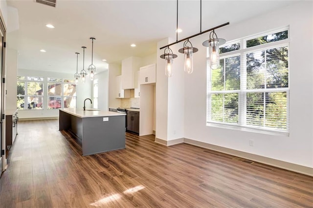 kitchen featuring white cabinets, decorative light fixtures, a healthy amount of sunlight, tasteful backsplash, and a kitchen island with sink