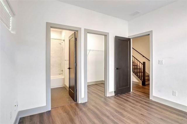 unfurnished bedroom with a spacious closet, a closet, connected bathroom, and hardwood / wood-style floors