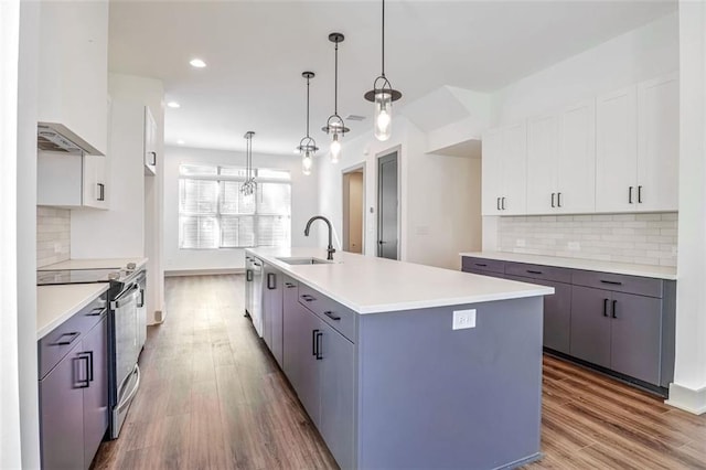 kitchen with an island with sink, electric stove, pendant lighting, white cabinets, and sink