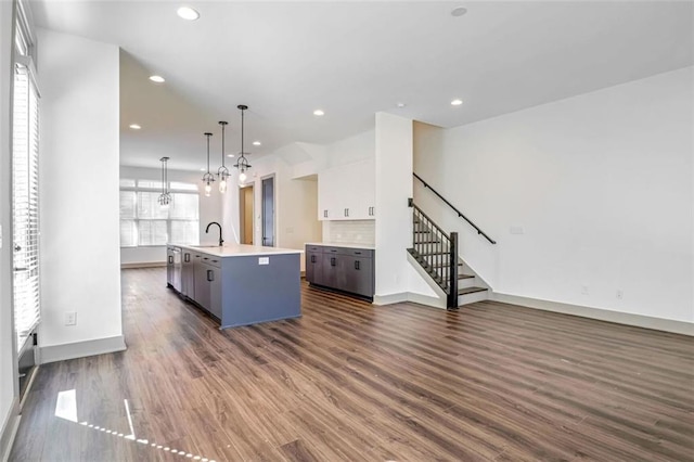 kitchen with white cabinetry, an island with sink, decorative light fixtures, dark wood-type flooring, and sink