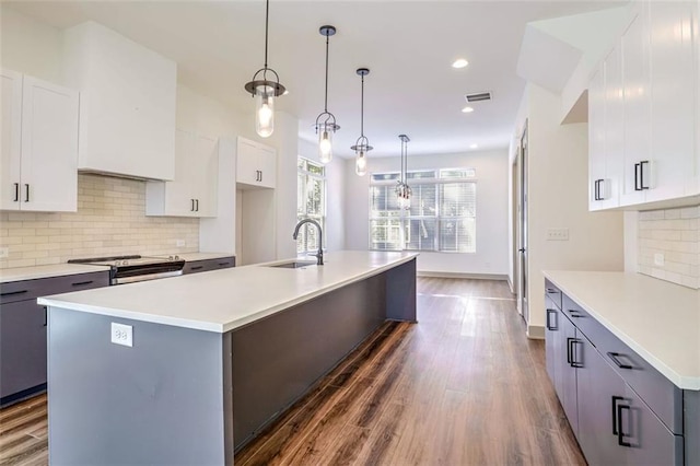 kitchen with electric stove, a center island with sink, hanging light fixtures, dark wood-type flooring, and white cabinets